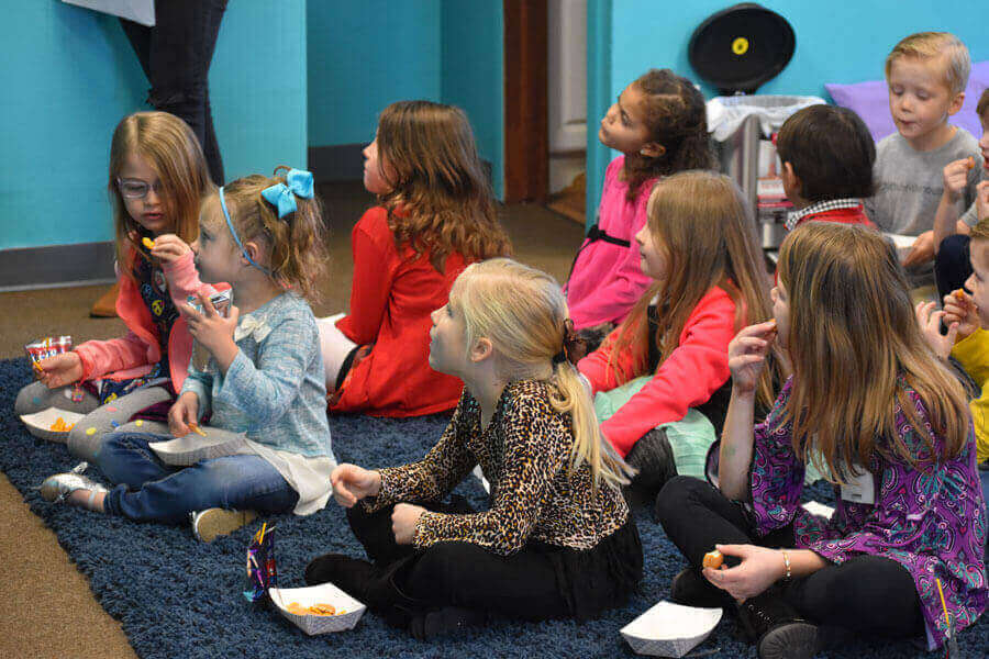 Group of children sitting on the floor, engaging in a group activity indoors.