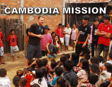 Group of people engaging in an outdoor community event with a sign that reads "cambodia mission."